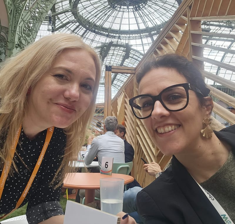 Two women taking a selfie at a meeting table under the glass dome of the Grand Palais at ChangeNOW 2026