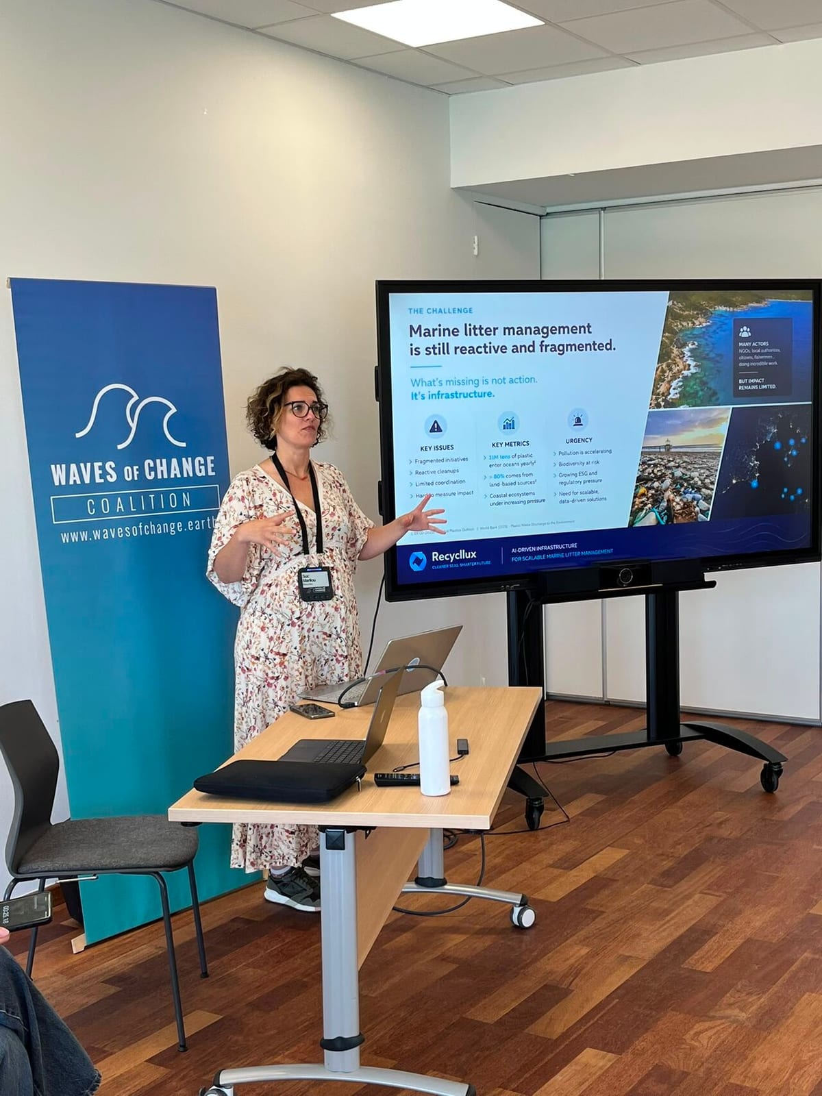 Presenter beside a Waves of Change Coalition banner and a screen reading Marine litter management is still reactive and fragmented