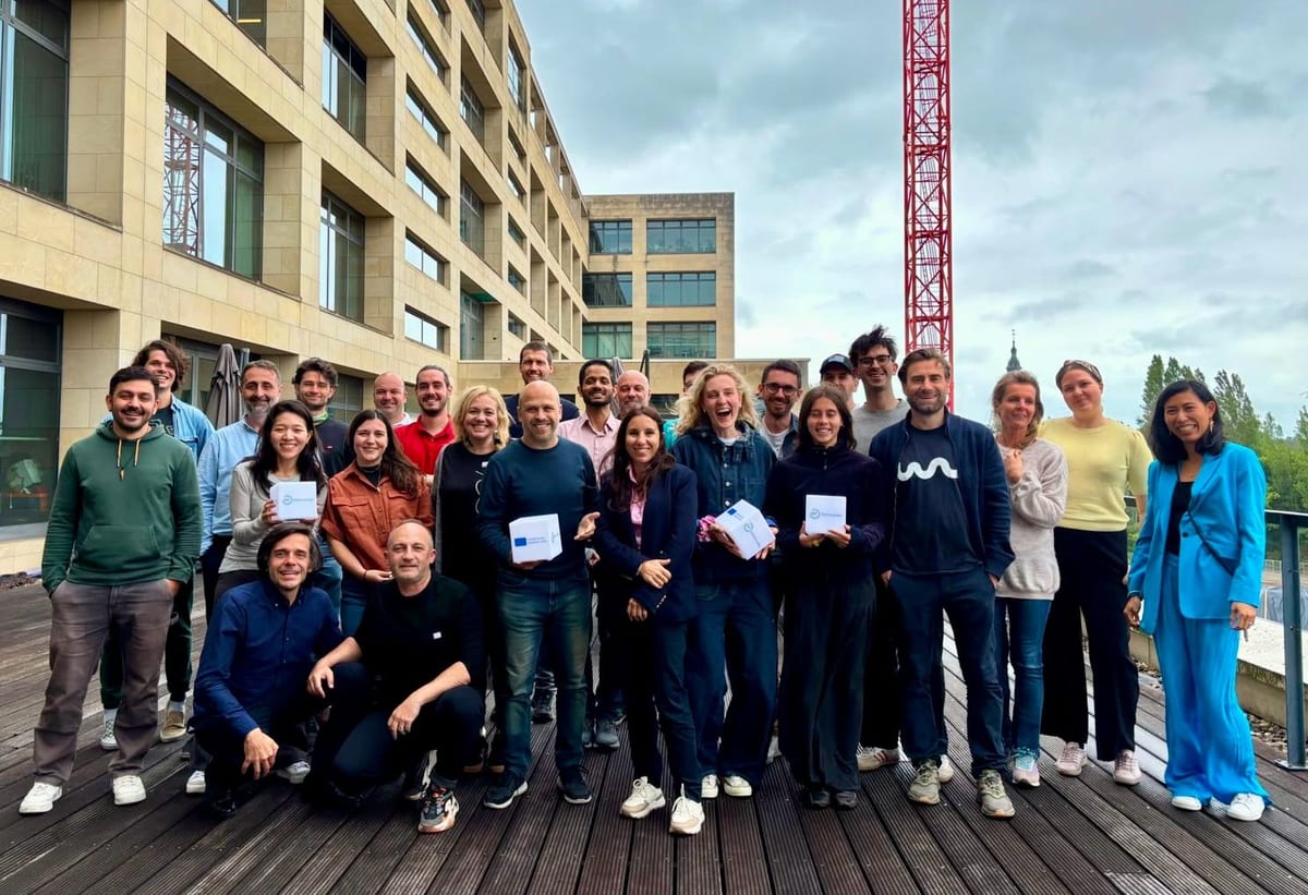 Catalyse NEB 2026 cohort members posing for a group photo on an outdoor terrace in Leuven, some holding small boxes